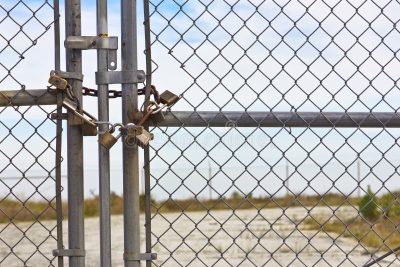 Multiple Padlocks used on a chain link fence with an old road on the backgr...