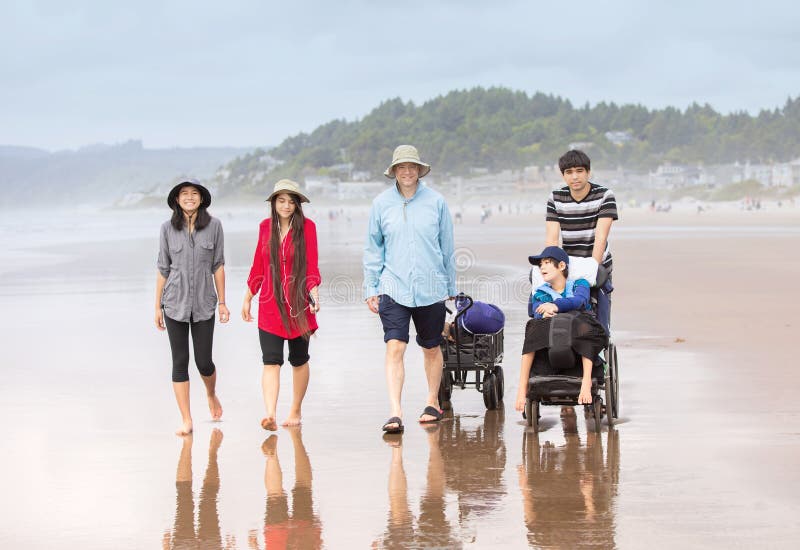 Multiracial Family walking on beach with disabled son in wheelchair