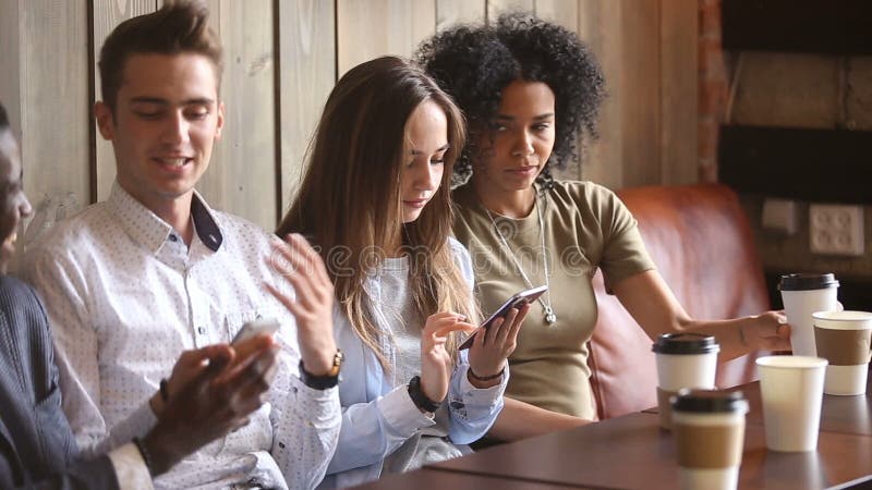 Multiracial friends using smartphones and talking in coffeehouse, mobile addiction