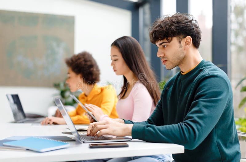 Multiracial male and female students studying for test, making homework with gadgets, focused guy using laptop stock photo