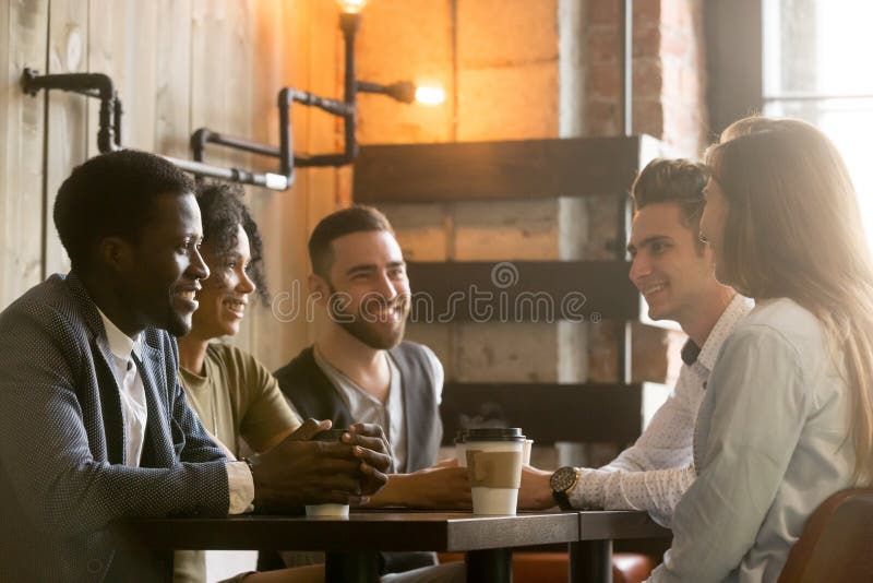 Multiraciale jonge vrienden die en koffie mede delen spreken drinken stock afbeelding Multiraciale jonge vrienden die en koffie mede delen spreken drinken stock afbeelding