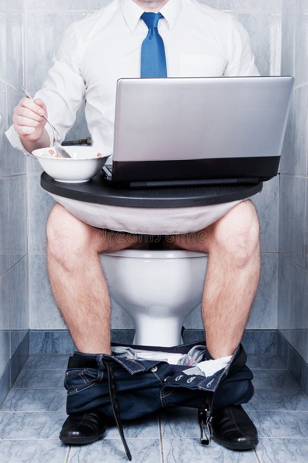 A man sitting in a toilet with a laptop and a bowl of soup royalty free sto...