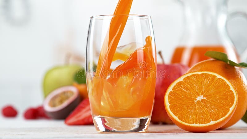 Multivitamin juice pouring into glass. Fresh orange juice with oranges fruit in kitchen