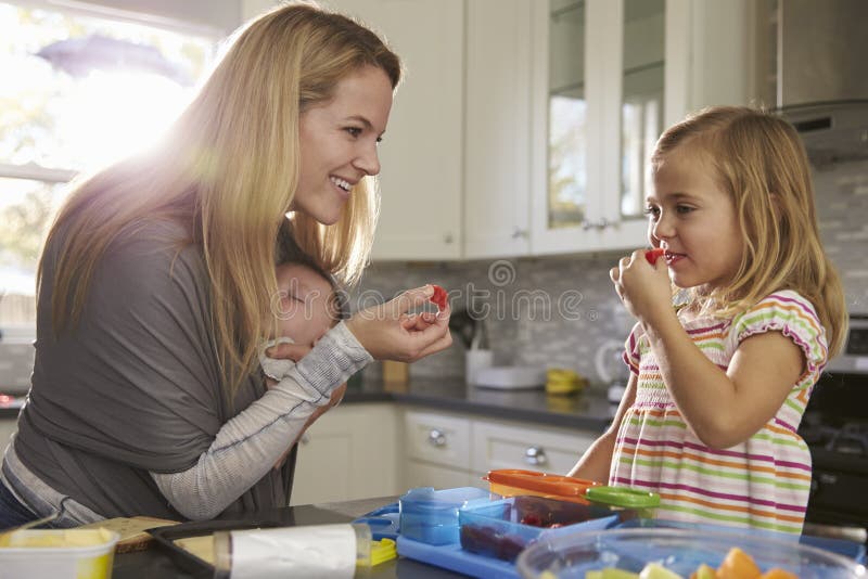 Mum and older daughter eating fruit, while baby sleeps in baby carrier