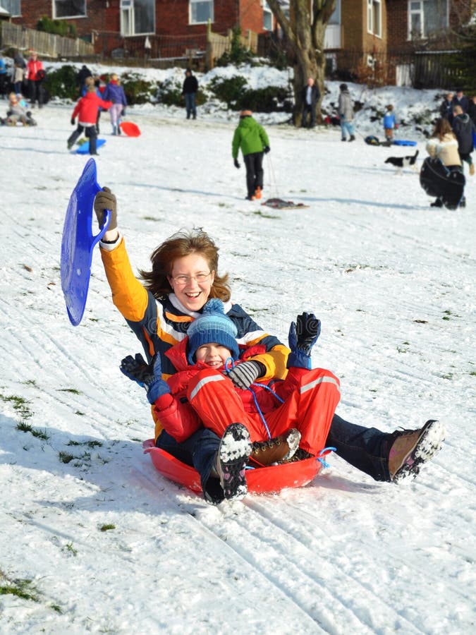 People having fun on snow: mother with youngster sliding a hill slope during bright sunny winter weekend in Meanwood Park, Leeds, United Kingdom. People having fun on snow: mother with youngster sliding a hill slope during bright sunny winter weekend in Meanwood Park, Leeds, United Kingdom.