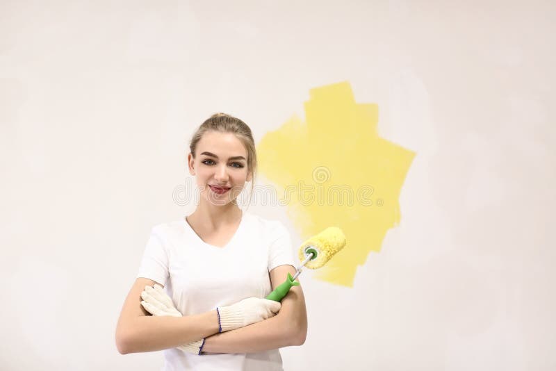 Mur femelle de peinture de décorateur avec le rouleau à l'intérieur photo stock Mur femelle de peinture de décorateur avec le rouleau à l'intérieur photo stock