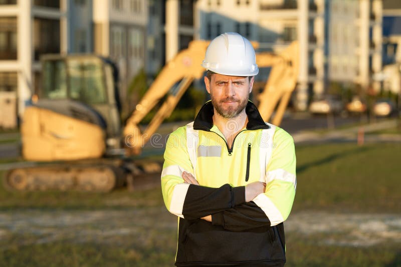 Muratore caucasico a casco nel cantiere. operaio di ingegneria industriale a hardhat vicino a bulldozer o immagini stock