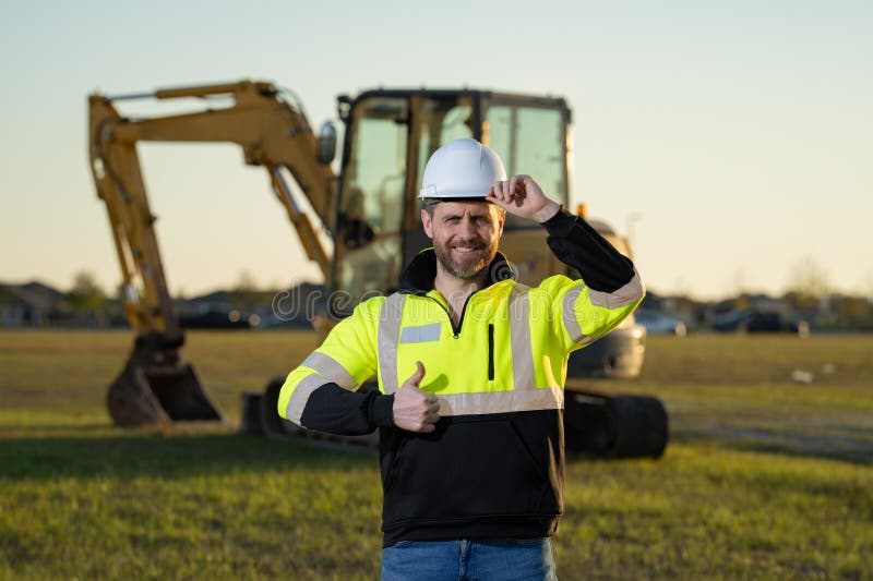Muratore caucasico a casco nel cantiere. operaio di ingegneria industriale a hardhat vicino a bulldozer o fotografia stock