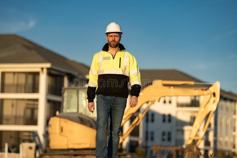 Muratore caucasico a casco nel cantiere. operaio di ingegneria industriale a hardhat vicino a bulldozer o fotografia stock libera da diritti