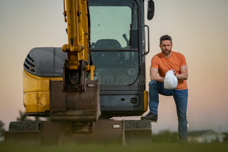 Muratore caucasico a casco nel cantiere. operaio di ingegneria industriale a hardhat vicino a bulldozer o fotografia stock libera da diritti