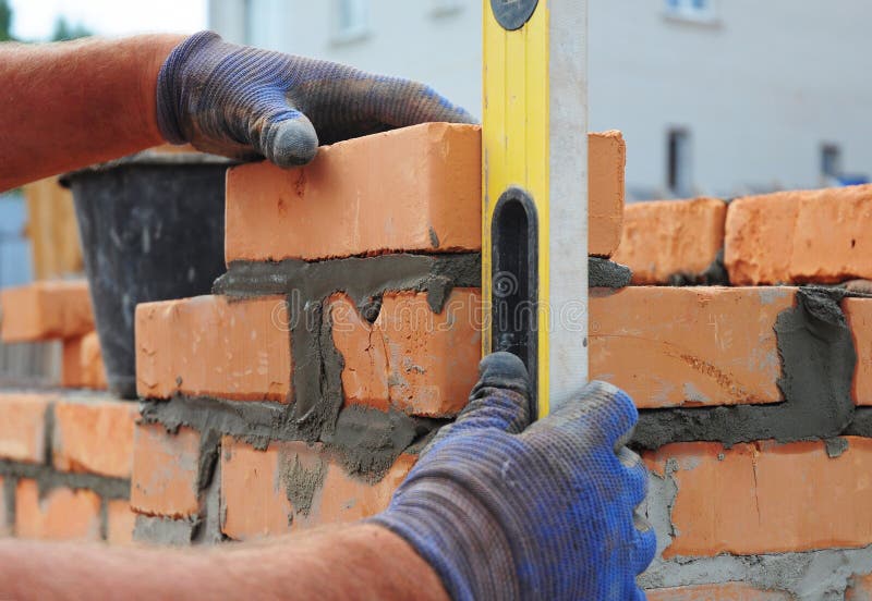 Bricklayer Using a Spirit Level to Check New Red Brick Wall Outdoor. Bricklayer Using a Spirit Level to Check New Red Brick Wall Outdoor.