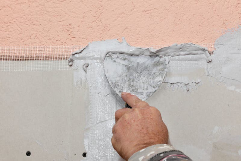 Worker spreading plaster with trowel to gypsum board and fiber mesh. Worker spreading plaster with trowel to gypsum board and fiber mesh