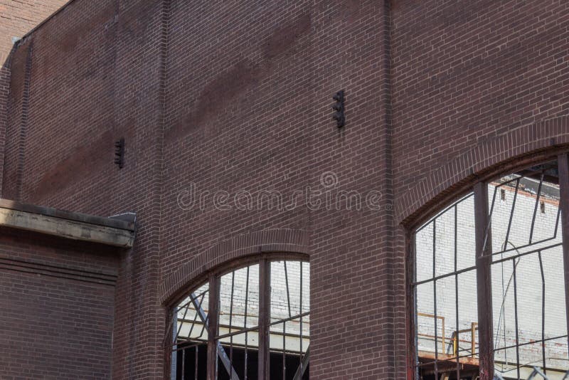 Muro di mattoni abbandonato con le strutture della finestra d'arrugginimento del metallo, nessun vetro del magazzino immagine stock Muro di mattoni abbandonato con le strutture della finestra d'arrugginimento del metallo, nessun vetro del magazzino immagine stock