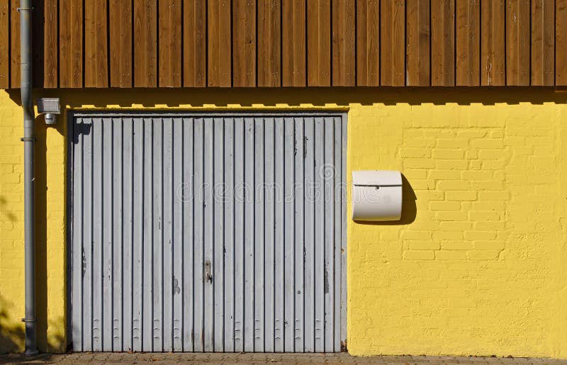 Muro di mattoni giallo con la porta del garage, la cassetta delle lettere, l'incanalamento e l'incorniciatura di legno sul second fotografia stock Muro di mattoni giallo con la porta del garage, la cassetta delle lettere, l'incanalamento e l'incorniciatura di legno sul second fotografia stock