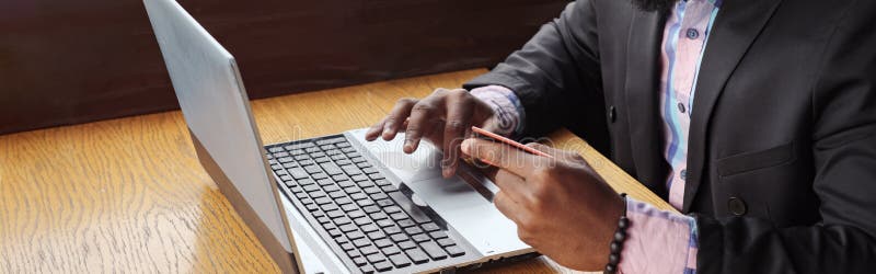 Murzyn robi płatniczej bank karcie na laptopie kupuje online, robiący zakupy siedzi w kawiarni zdjęcia royalty free Murzyn robi płatniczej bank karcie na laptopie kupuje online, robiący zakupy siedzi w kawiarni zdjęcia royalty free