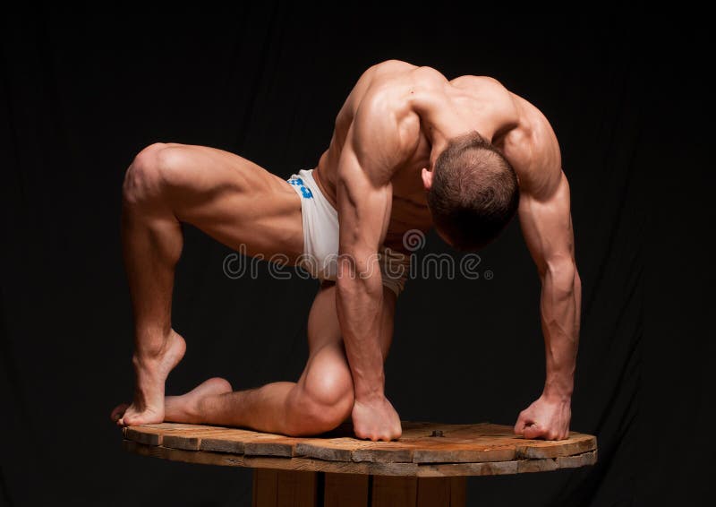 Muscolare giovane uomo in posa su una piattaforma di legno su sfondo nero.