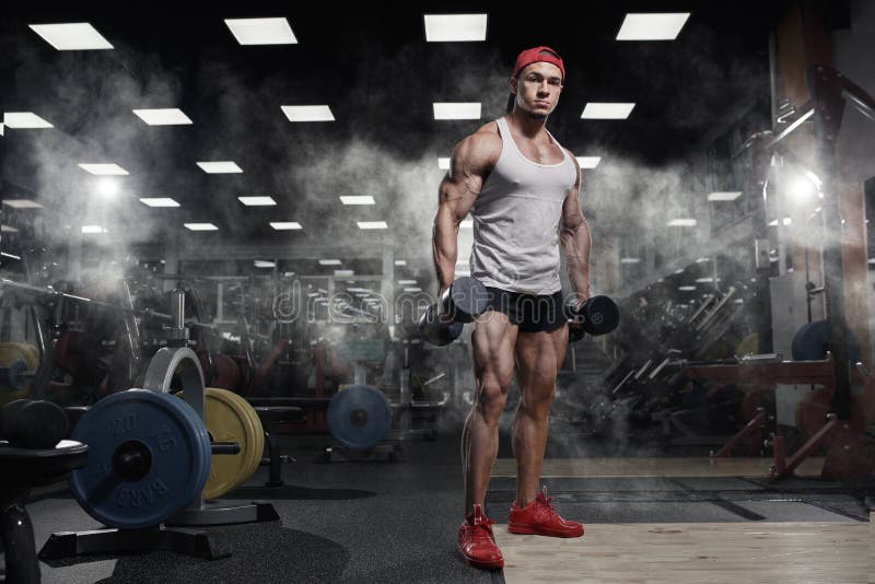 Muscular athletic bodybuilder fitness model training arms in gym. Man with great physique prepares for biceps workout in gym. Muscular athletic bodybuilder fitness model training arms in gym. Man with great physique prepares for biceps workout in gym