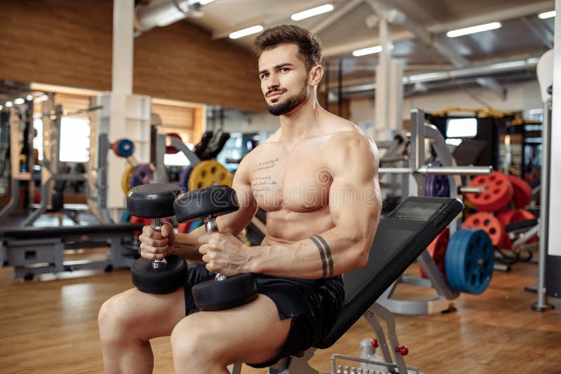 Muscular athletic young man bodybuilder fitness model focusing on exercise with dumbbell in the gym. stock photo Muscular athletic young man bodybuilder fitness model focusing on exercise with dumbbell in the gym. stock photo