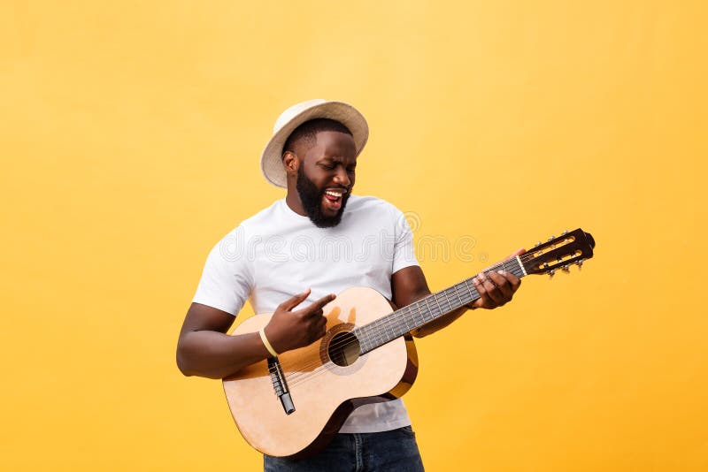 Muscular black man playing guitar, wearing jeans and white tank-top. Isolate over yellow background.