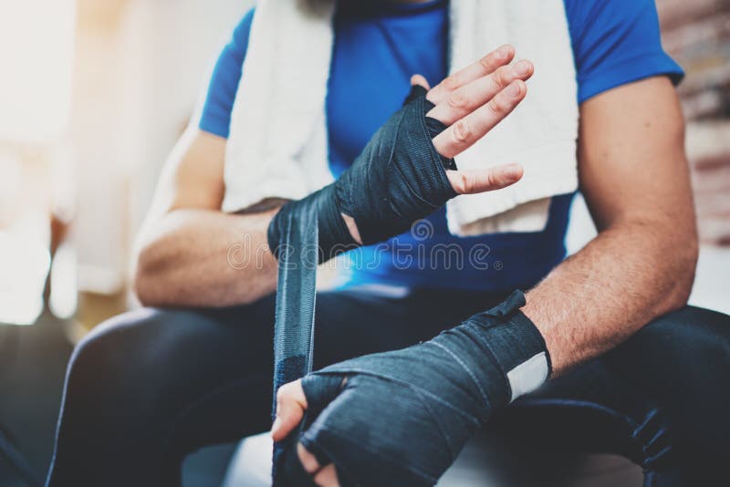 Muscular Boxer man prepairing hands for hard kickboxing training session in gym. Young athlete tying black boxing stock photos Muscular Boxer man prepairing hands for hard kickboxing training session in gym. Young athlete tying black boxing stock photos