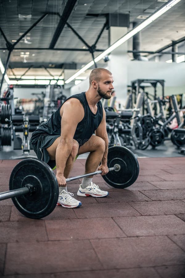 Muscular fitness man preparing to deadlift a barbell over his head in modern fitness center.Functional training.Snatch exercise.