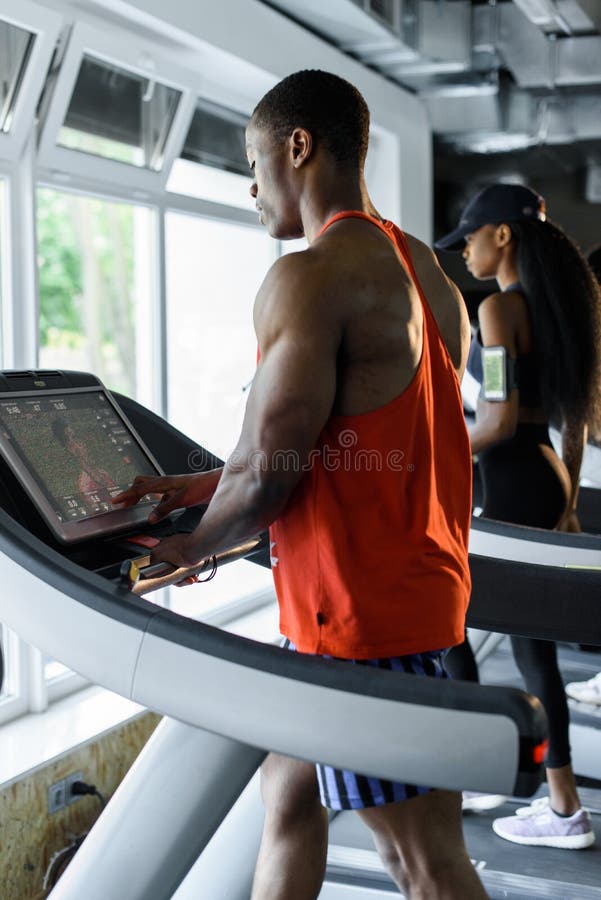 Muscular handsome black bodybuilder jogging on a treadmill in the gym stock image