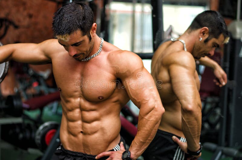 Muscular, shirtless male bodybuilder resting in gym during workout showing muscular torso, pecs and abs. Muscular, shirtless male bodybuilder resting in gym during workout showing muscular torso, pecs and abs