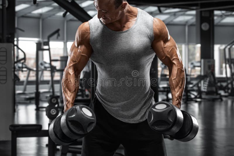 Muscular man with dumbbells in gym. Strong male bodybuilder working out