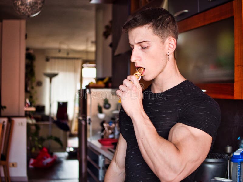 Muscular Young Man Eating Cereal Bar, Looking at Camera Standing, Stock