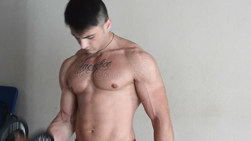 Muscular young man exercising biceps with dumbbells