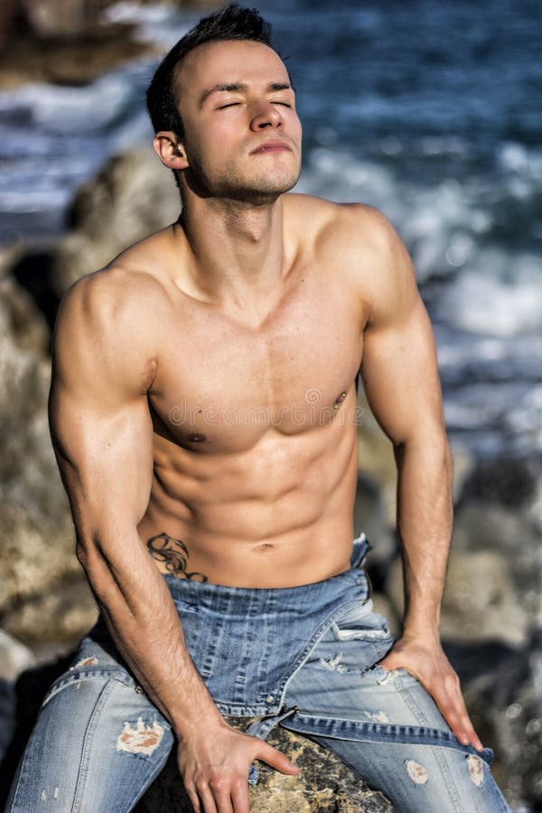 Muscular young man sunbathing on rock by sea