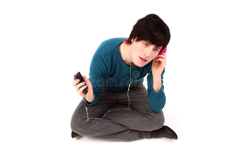 Listening to music on mp3 or ipod player with headphones. Male with black and purple hair in jeans with blue top and white belt. Gay guy with fashion clothes. Listening to music on mp3 or ipod player with headphones. Male with black and purple hair in jeans with blue top and white belt. Gay guy with fashion clothes