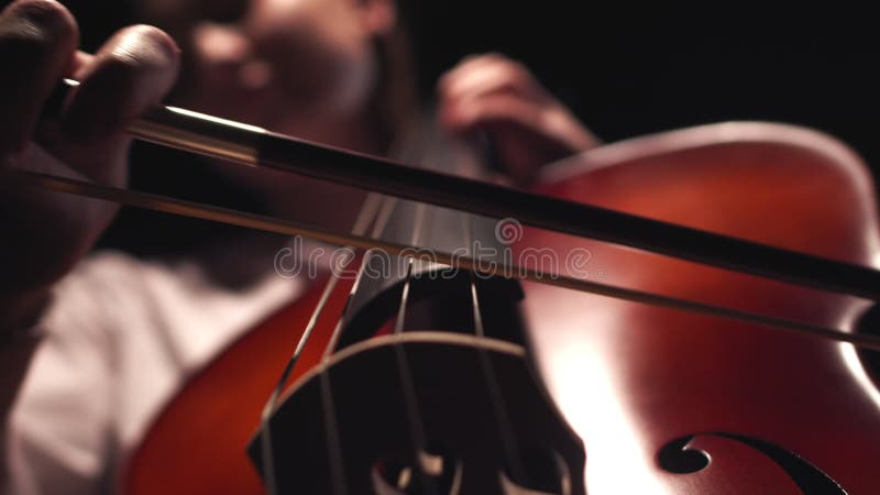 Musician leads bow along strings of cello playing classical music, closeup, front view. Musician performs playing stock video footage