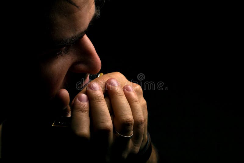 Brunette man playing on harmonica on dark background with place for your text. Brunette man playing on harmonica on dark background with place for your text