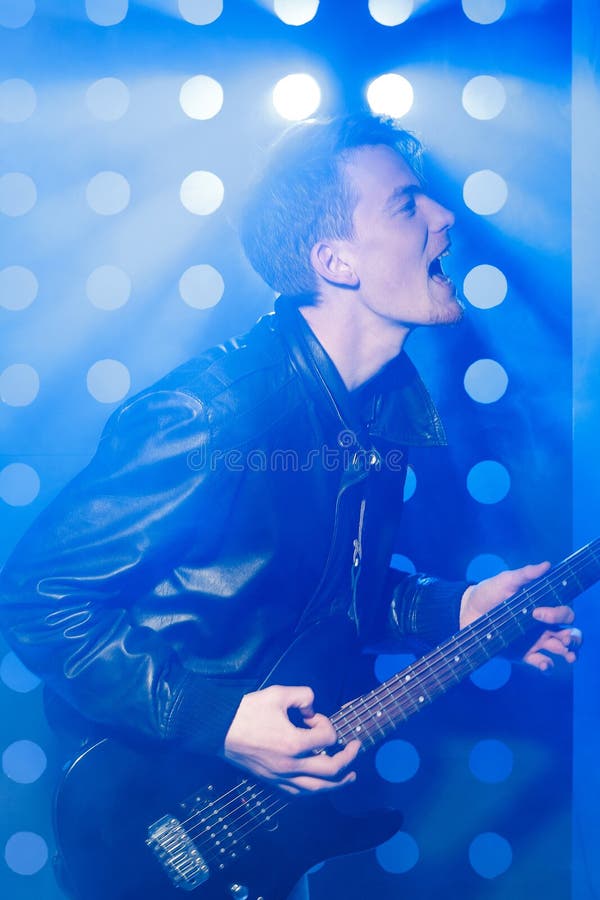 Musicista della roccia dei giovani che gioca chitarra elettrica e che canta Rock star su fondo dei riflettori fotografie stock libere da diritti Musicista della roccia dei giovani che gioca chitarra elettrica e che canta Rock star su fondo dei riflettori fotografie stock libere da diritti