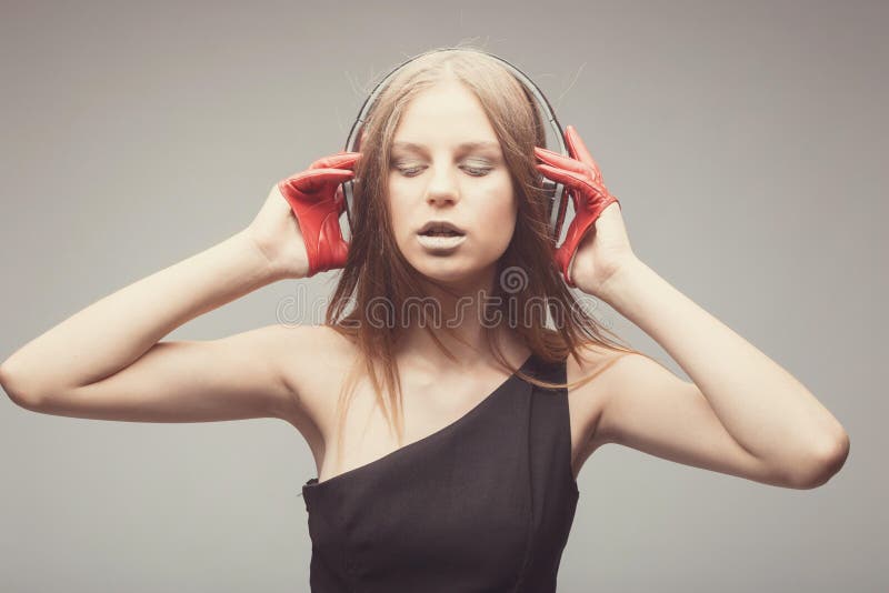 Musik för nätt flicka för mode lyssnande med hörlurar, bärande röda handskar, nära ögon och att ta nöje med sång fotografering för bildbyråer Musik för nätt flicka för mode lyssnande med hörlurar, bärande röda handskar, nära ögon och att ta nöje med sång fotografering för bildbyråer