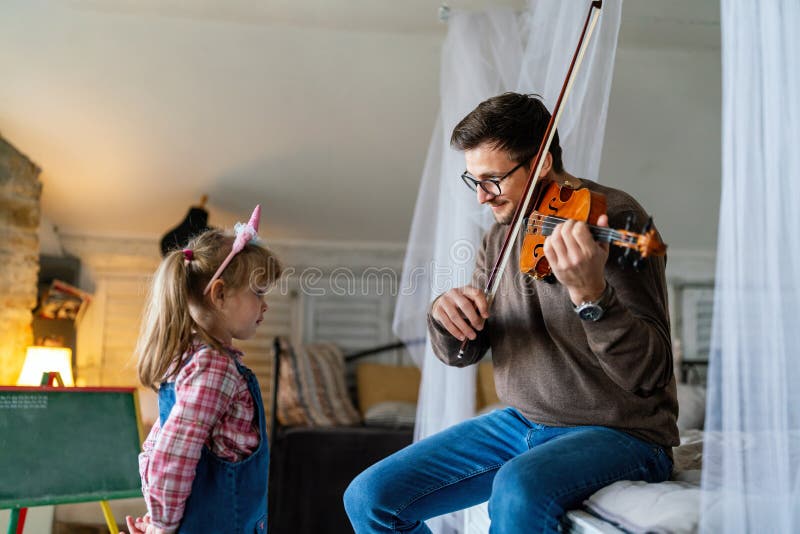 Musik är så kul. Ung far som undervisar sin lilla dotter att spela fiolin och le. arkivbilder