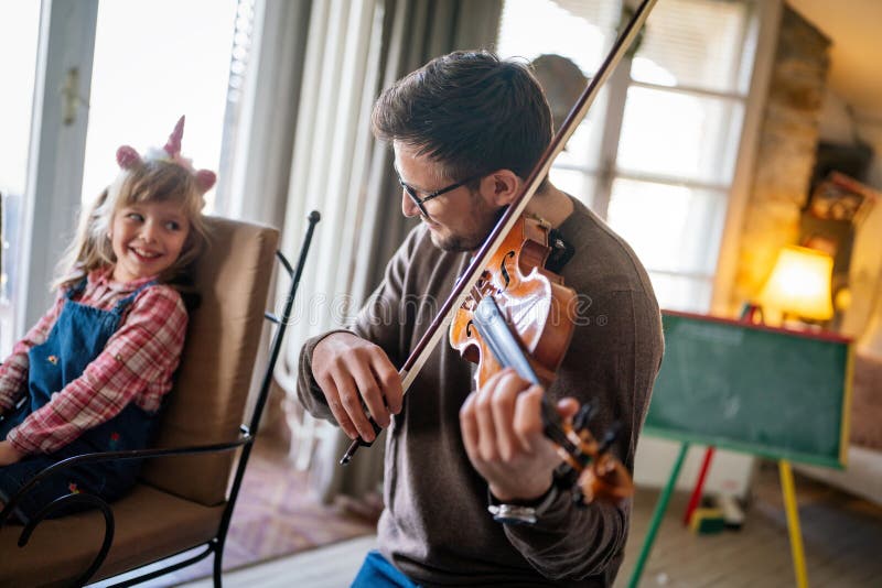 Musiken är så kul. Ung far som undervisar sin lilla dotter att spela fiolin och le. royaltyfri foto