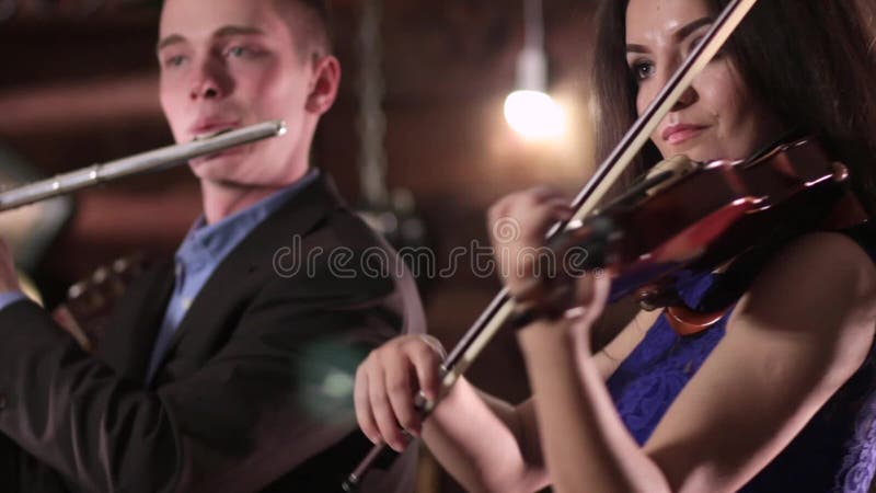 Musiker mit zwei Leuten, der Musik spielt Ein schöner Brunette in einem blauen Kleid spielt die Violine und den Kerl in der Jacke