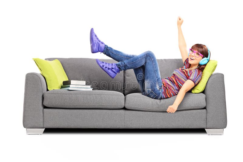 Musique de écoute femelle excitée par jeunes posée sur un sofa photographie stock Musique de écoute femelle excitée par jeunes posée sur un sofa photographie stock
