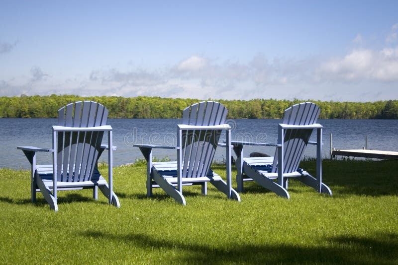Three Red Muskoka Chairs on a Dock Looking Out into the Lake Stock