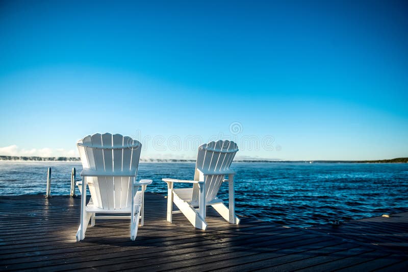 Muskoka-Stühle auf einem Dock mit dem Sonnensteigen und -nebel