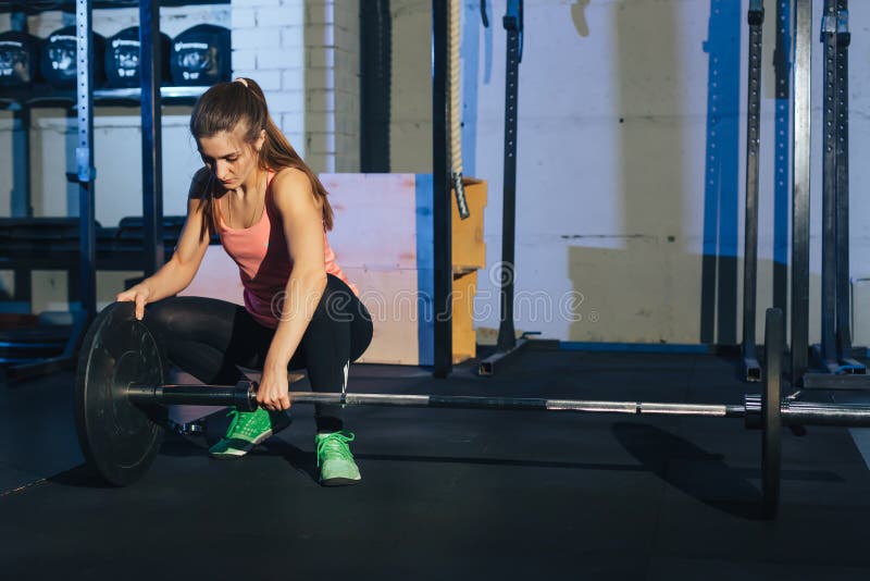 Muskulös ung konditionkvinna som lyfter en viktcrossfit i idrottshallen Skivstång för konditionkvinnadeadlift Idrottshallen på de royaltyfri bild Muskulös ung konditionkvinna som lyfter en viktcrossfit i idrottshallen Skivstång för konditionkvinnadeadlift Idrottshallen på de royaltyfri bild