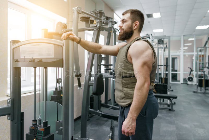 Portrait muscular caucasian bearded man dressed in weighted vest in the gym, military style. Portrait muscular caucasian bearded man dressed in weighted vest in the gym, military style.