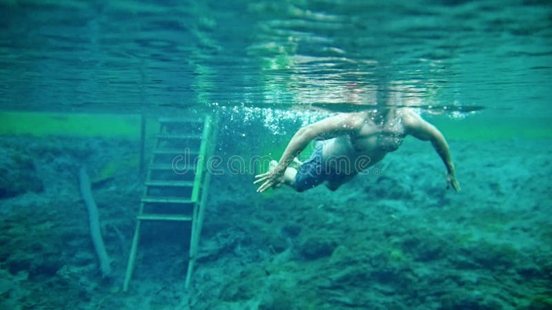 Muskulöser Mann, der unter Wasser im klaren blauen See schwimmt