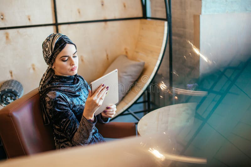 Muslim business woman with beautiful smile holding digital tablet while sitting in cafe. Muslim business woman with beautiful smile holding digital tablet while sitting in cafe