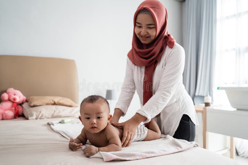 Asian muslim mother giving massage to her baby toddler on the bed