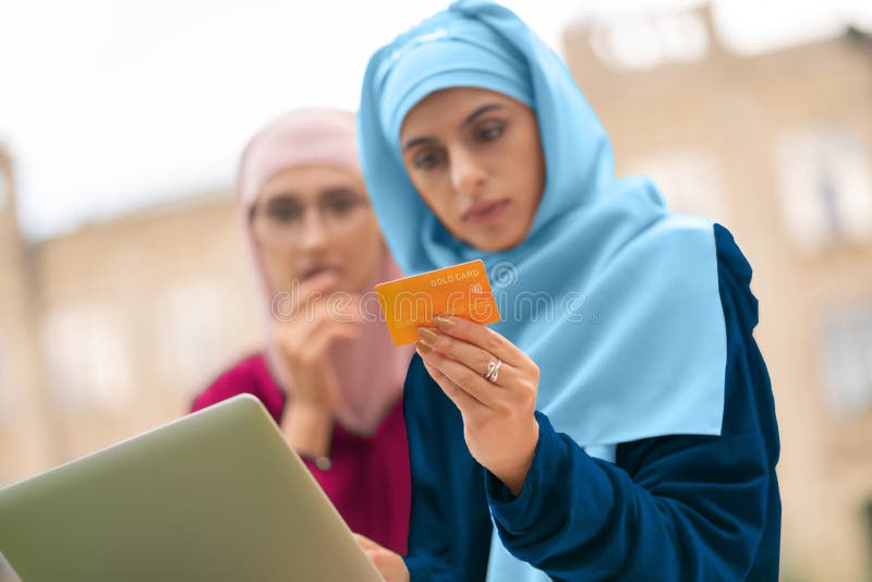 Muslim women holding bank card while shopping online. Holding bank card. Two young muslim women holding bank card while shopping online outside royalty free stock images Muslim women holding bank card while shopping online. Holding bank card. Two young muslim women holding bank card while shopping online outside royalty free stock images