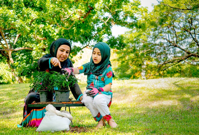 Muslimsk moderhjälp och att undervisa hennes dotter att växa och plantera ett träd i trädgården arkivbild Muslimsk moderhjälp och att undervisa hennes dotter att växa och plantera ett träd i trädgården arkivbild