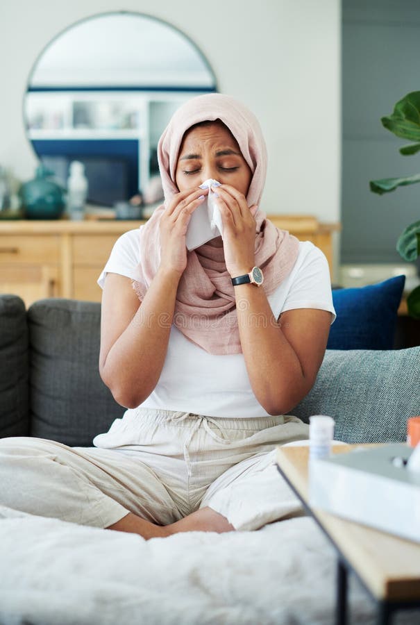 Muslim, woman and sick or sneezing on couch in living room with illness, flu and tired at home. Female person, lounge and fever with medication to relax, chill and calm on sofa for recovery or rest. Muslim, woman and sick or sneezing on couch in living room with illness, flu and tired at home. Female person, lounge and fever with medication to relax, chill and calm on sofa for recovery or rest.